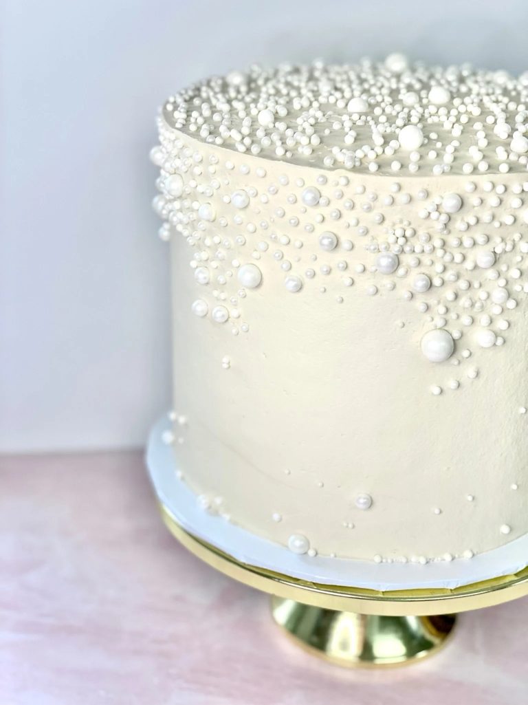 Elegant ivory wedding cake adorned with cascading pearl decorations on gold cake stand