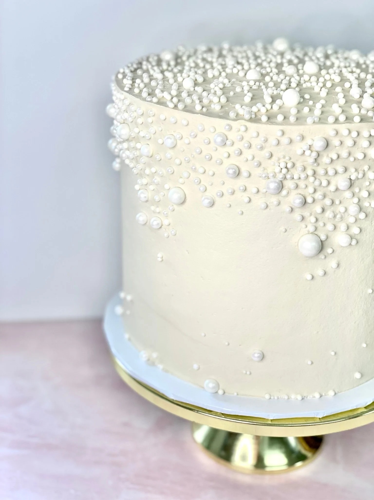Elegant ivory wedding cake adorned with cascading pearl decorations on gold cake stand