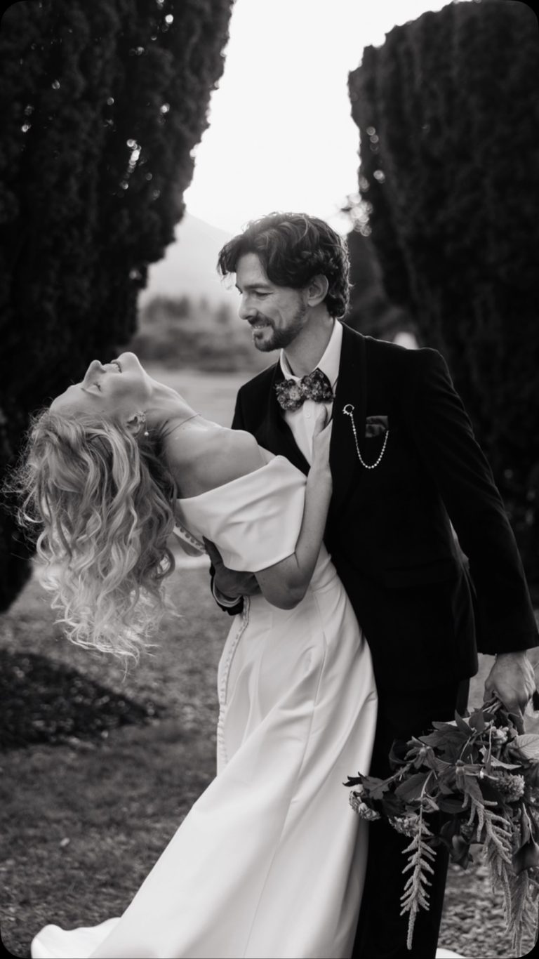 Bride and groom dancing together in elegant black and white photograph with cypress trees framing the romantic moment