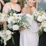 Smiling bride in white strapless gown with bridesmaid holding lush white and green bouquets
