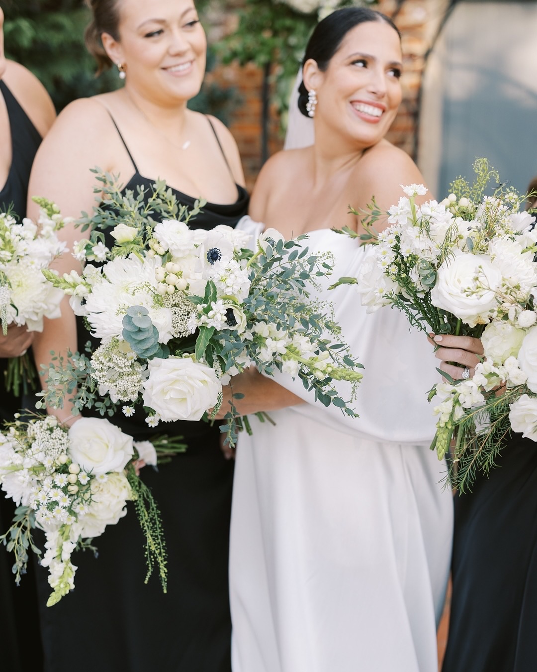 Smiling bride in white strapless gown with bridesmaid holding lush white and green bouquets