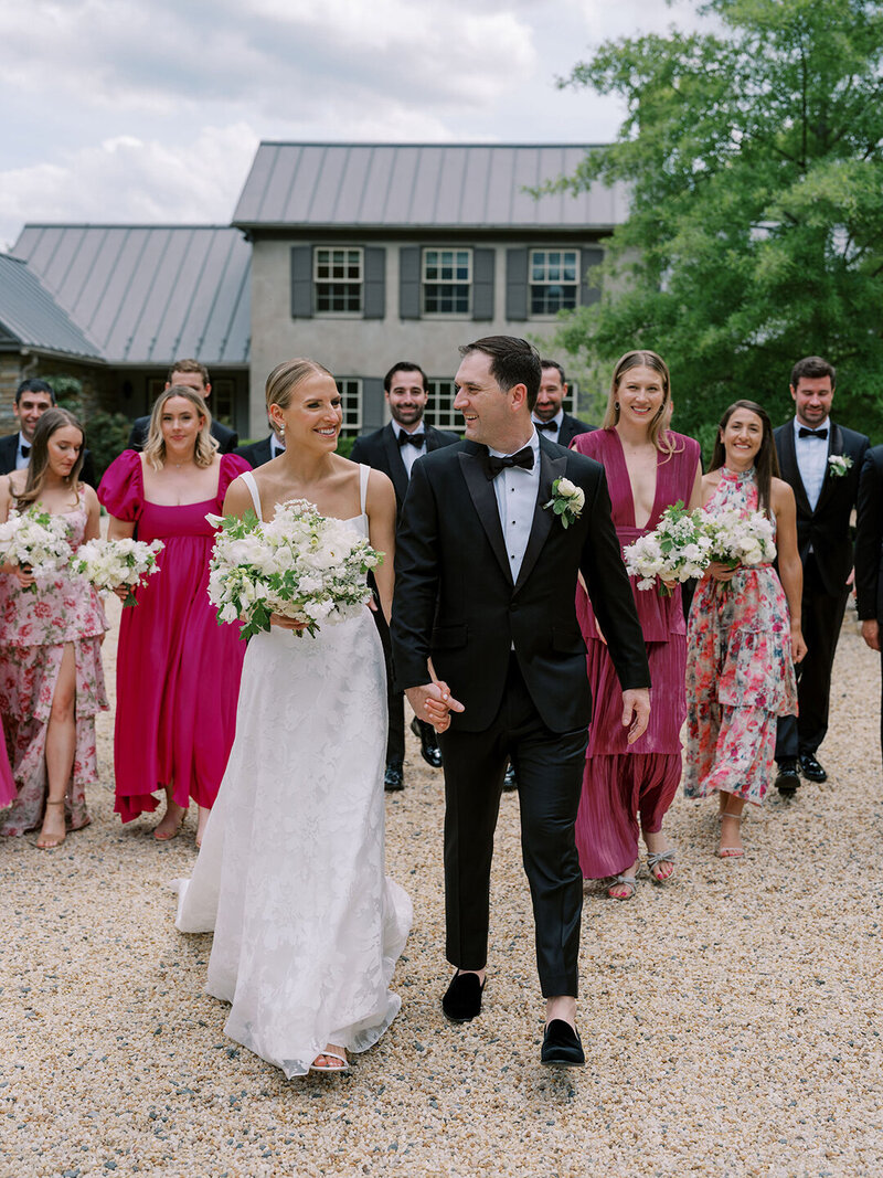 Joyful newlyweds with bridesmaids in pink gowns and groomsmen in tuxedos at outdoor wedding celebration