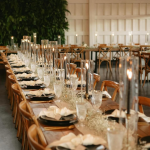 Long wooden banquet tables with cross-back chairs, tall cylinder candles, and baby's breath garland for wedding reception