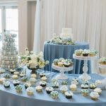 Wedding dessert display with blue and white themed cupcakes, macaron tower, and tiered cake on elegant stands