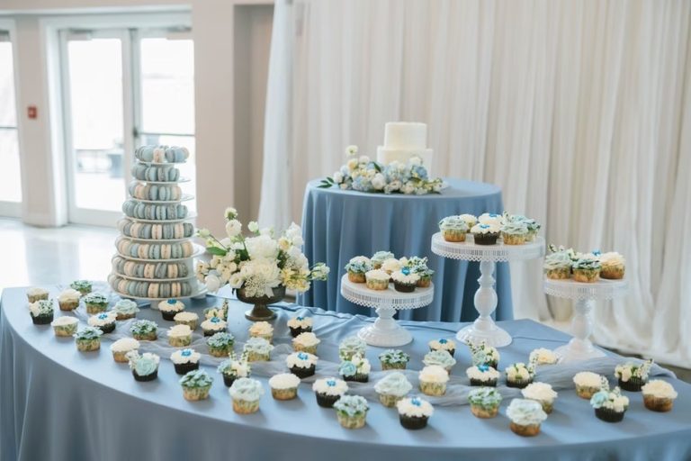 Wedding dessert display with blue and white themed cupcakes, macaron tower, and tiered cake on elegant stands