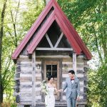 bride and groom standing in front of log cabin chapel