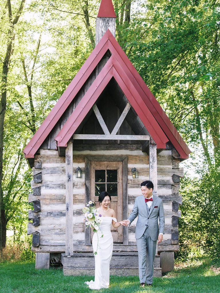 bride and groom standing in front of log cabin chapel