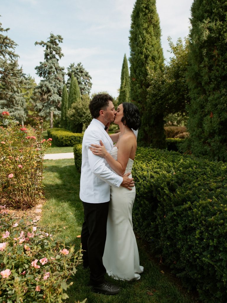 Bride and groom share romantic kiss among manicured gardens and flowering roses