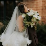 Bride in white ball gown and veil smelling white calla lily bouquet outdoors at brick building