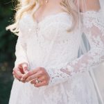 Bride in lace wedding dress with long sleeves and veil, engagement ring visible on hand