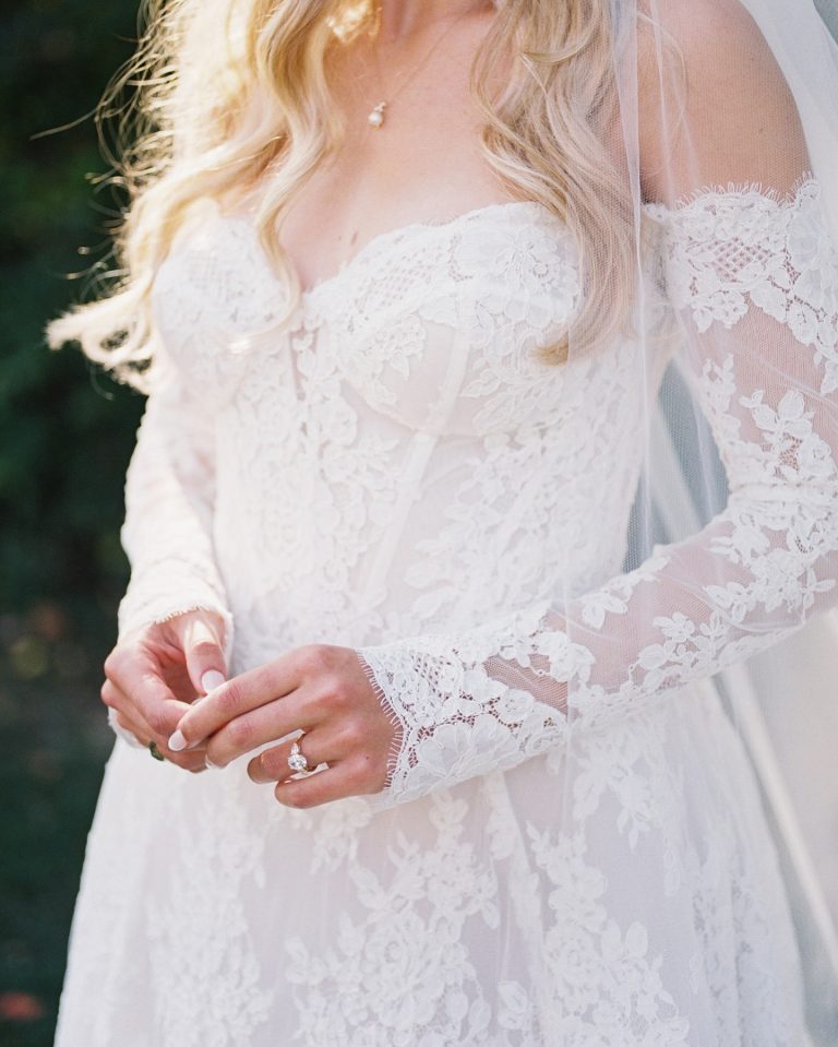 Bride in lace wedding dress with long sleeves and veil, engagement ring visible on hand