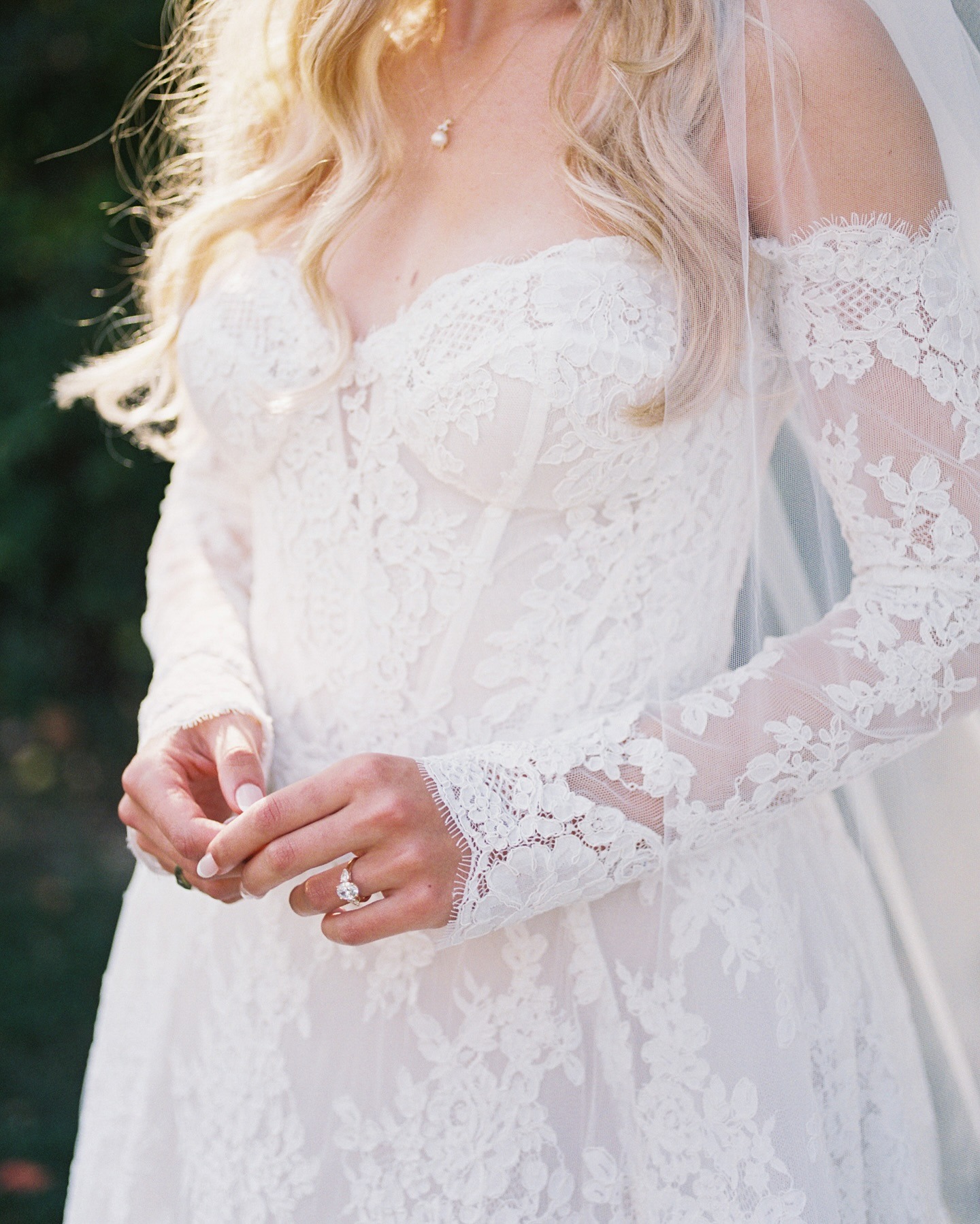 Bride in lace wedding dress with long sleeves and veil, engagement ring visible on hand