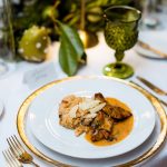 Elegant plated dinner with risotto, chicken, and parmesan on gold-rimmed china with green glassware centerpiece