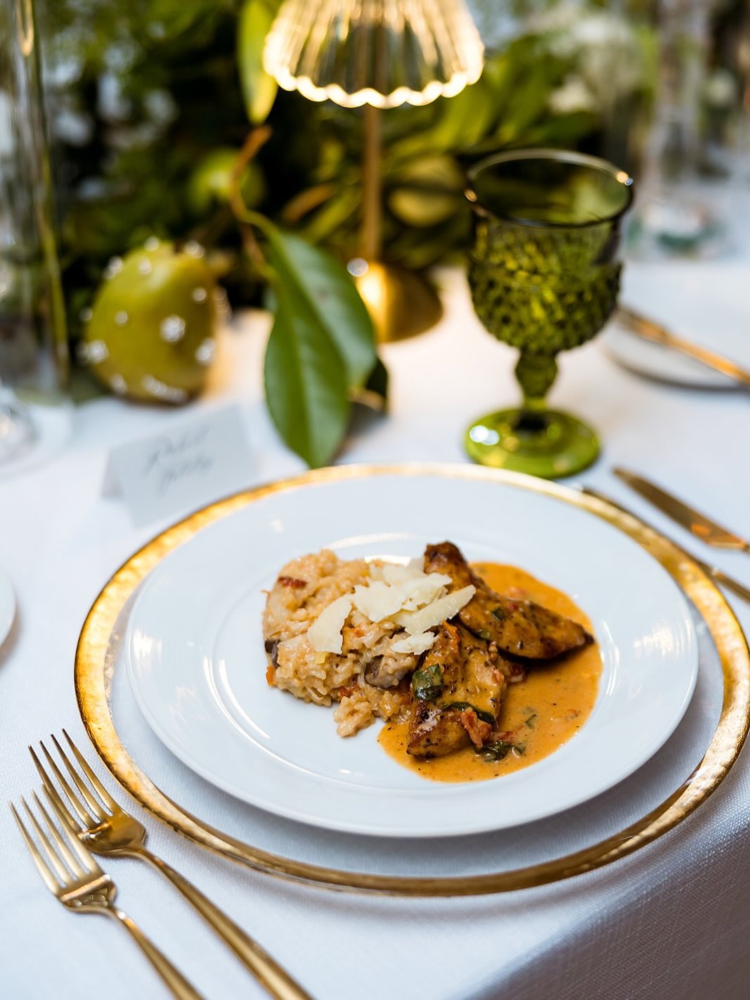 Elegant plated dinner with risotto, chicken, and parmesan on gold-rimmed china with green glassware centerpiece