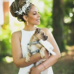 Bride with braided updo and floral crown holding small dog outdoors in natural light