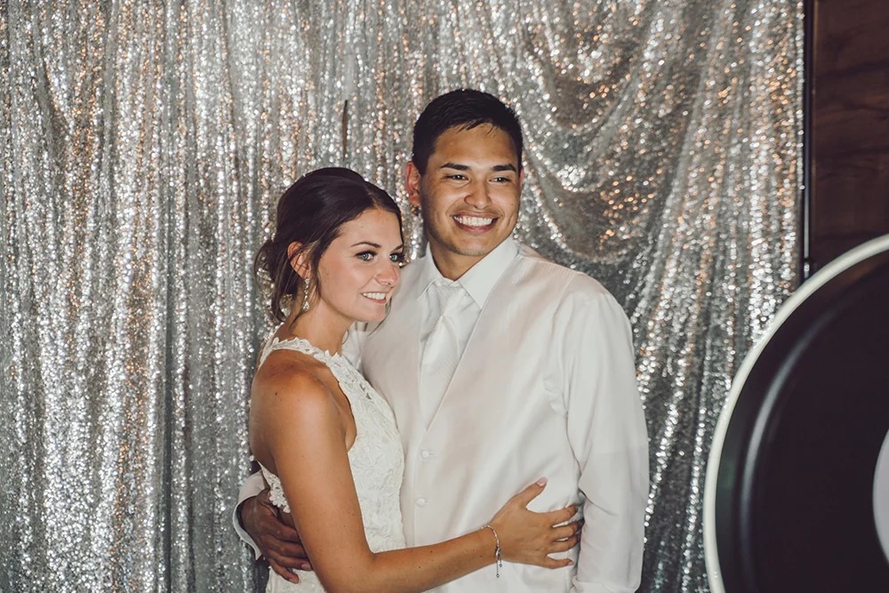 Bride and groom posing in photo booth with silver sequin backdrop
