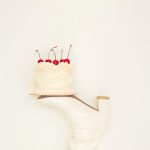 Two-tier white frosted wedding cake topped with maraschino cherries on a white cake stand