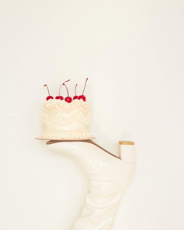 Two-tier white frosted wedding cake topped with maraschino cherries on a white cake stand