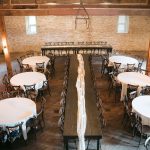 Aerial view of barn interior wedding setup featuring limestone walls, wooden floors, draped ceremony aisle, and reception tables