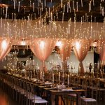 Romantic candlelit reception in warehouse venue featuring long farmhouse tables and theatrical floating candle installation
