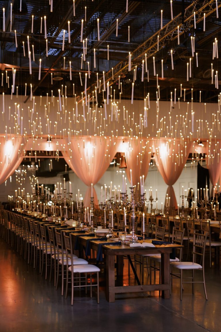 Romantic candlelit reception in warehouse venue featuring long farmhouse tables and theatrical floating candle installation