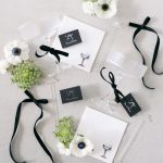 Elegant wedding welcome gifts with clear tumblers, white anemones, greenery, and black ribbon on white envelopes