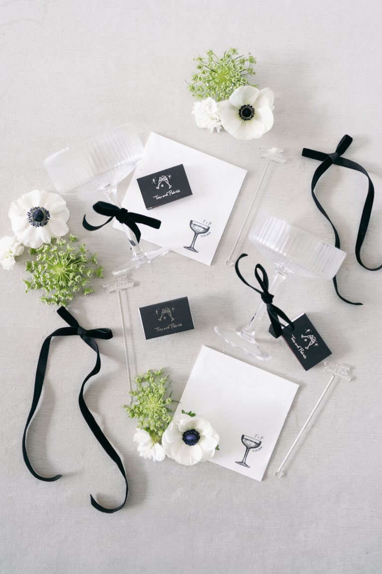 Elegant wedding welcome gifts with clear tumblers, white anemones, greenery, and black ribbon on white envelopes