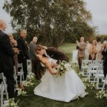 Outdoor wedding ceremony with couple walking down aisle lined with white chairs and guests