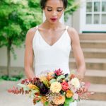 Bride in minimalist white V-neck gown holding colorful fall bouquet with peach roses, eucalyptus, and burgundy blooms