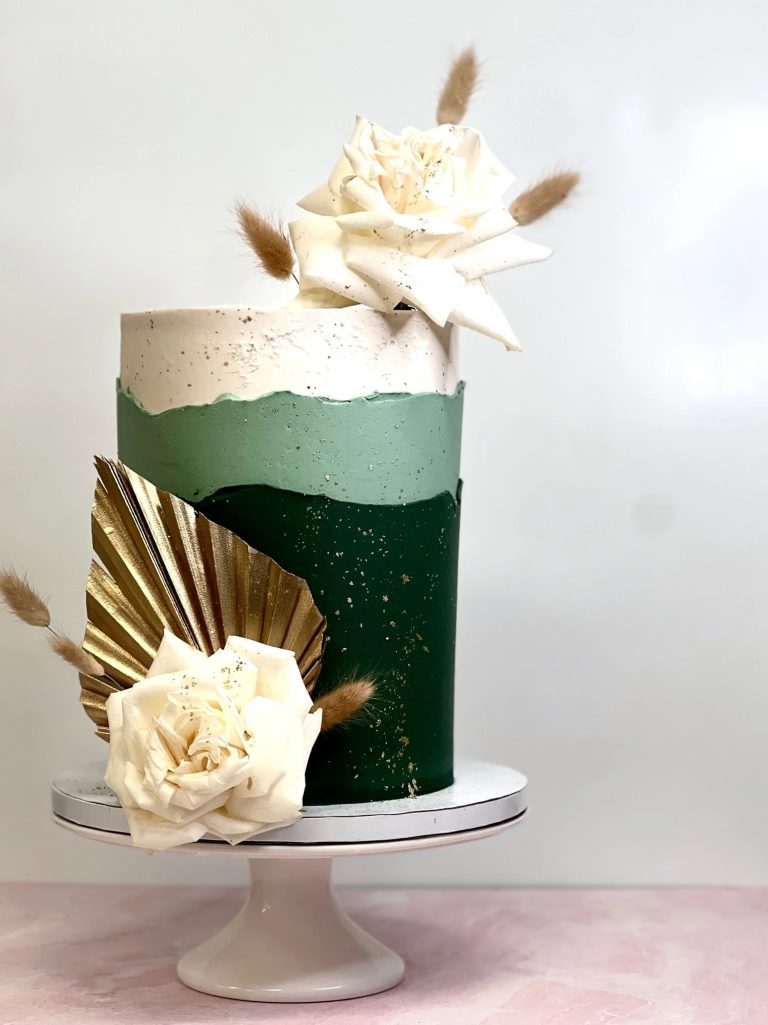 Single-tier wedding cake with ombre green frosting, ivory sugar flowers, gold palm leaf accent, and pampas grass