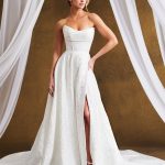 Bride in strapless A-line wedding gown with high front slit and cathedral train, framed by white draping against gold backdrop