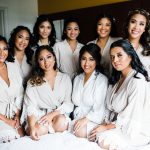 Bride and bridesmaids in white robes with professional hair and makeup styling on wedding day