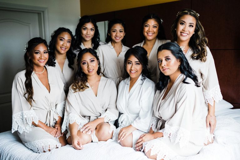 Bride and bridesmaids in white robes with professional hair and makeup styling on wedding day