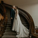 Bride in lace gown descending curved wooden staircase