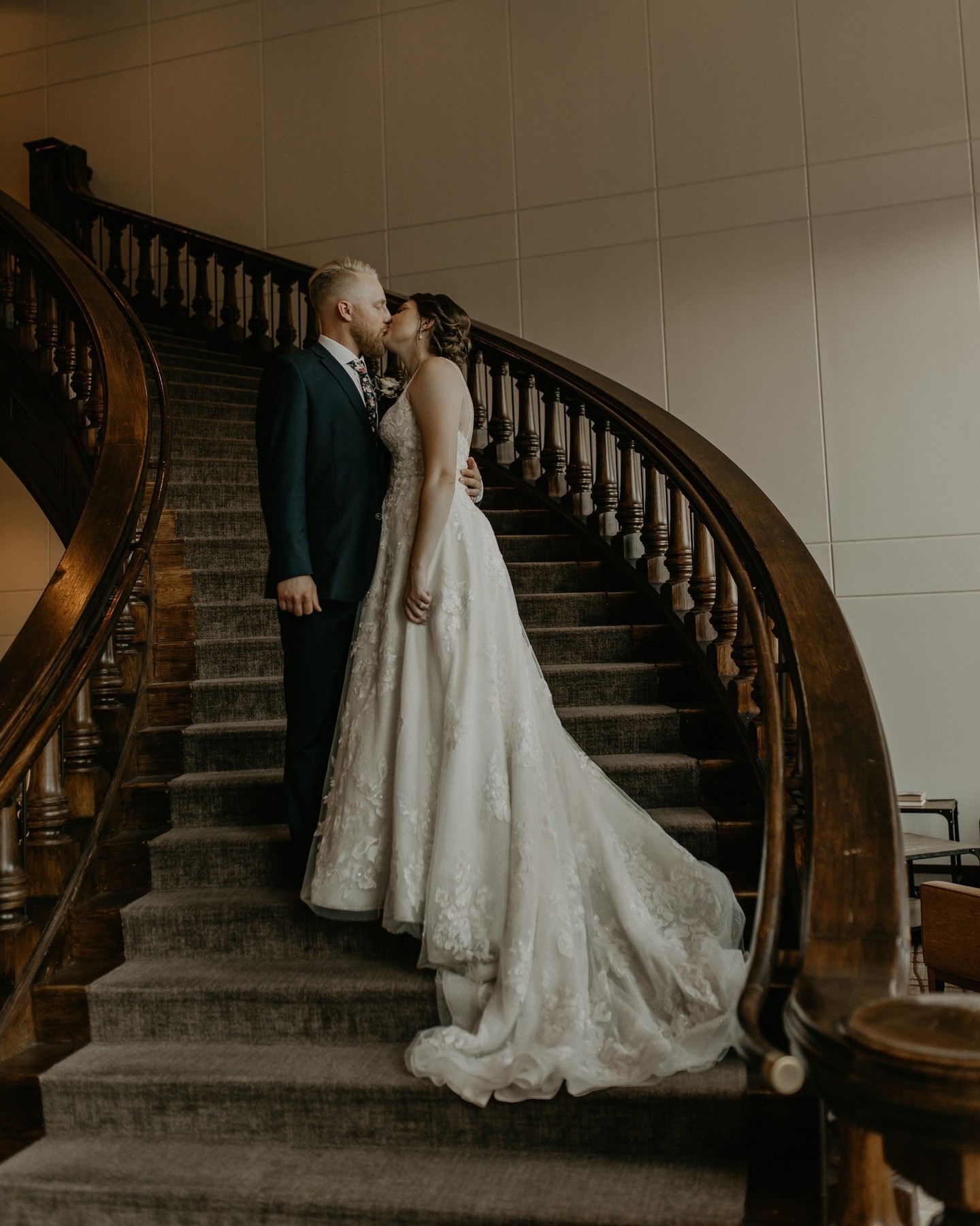 Bride in lace gown descending curved wooden staircase