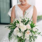 Bride in lace gown holding lush white and blush bouquet with trailing greenery