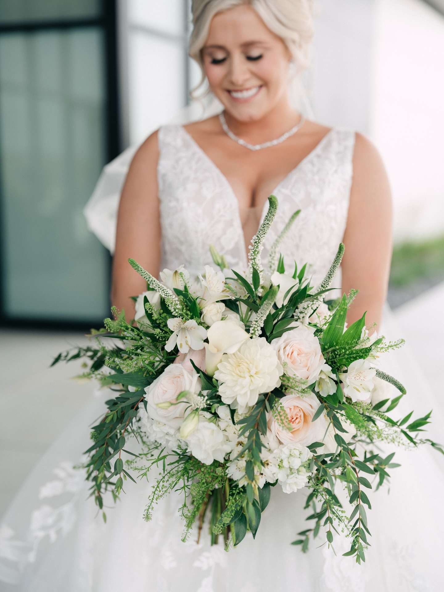 Bride in lace gown holding lush white and blush bouquet with trailing greenery