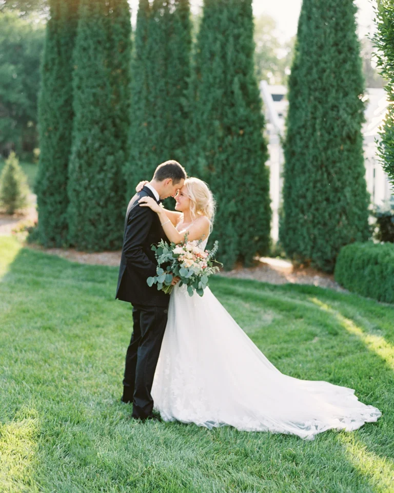 Bride and groom share intimate moment in garden with row of cypress trees