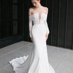 Bride in sleek white mermaid gown with dramatic off-shoulder sleeves and flowing train