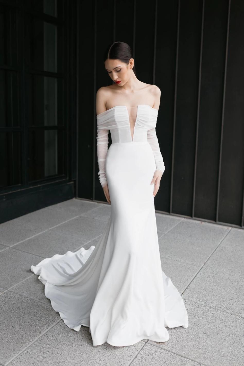 Bride in sleek white mermaid gown with dramatic off-shoulder sleeves and flowing train