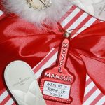 Custom red Motel Mansur ornament with Austin, TX date next to Louis Vuitton slipper on striped gift wrap