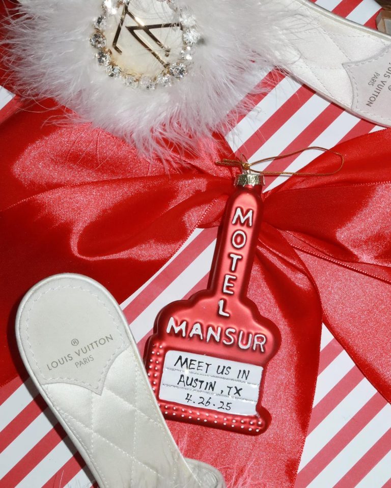 Custom red Motel Mansur ornament with Austin, TX date next to Louis Vuitton slipper on striped gift wrap