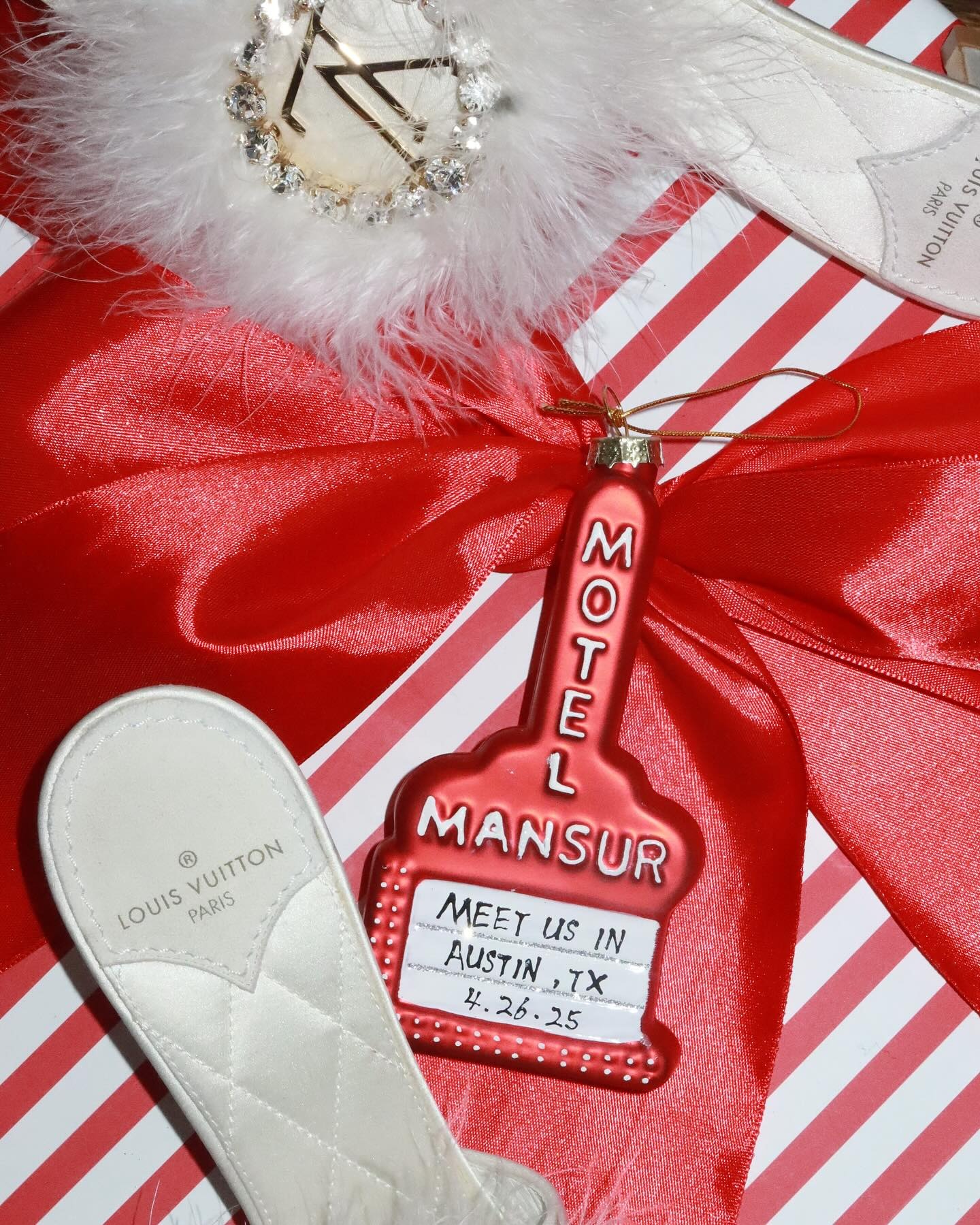 Custom red Motel Mansur ornament with Austin, TX date next to Louis Vuitton slipper on striped gift wrap