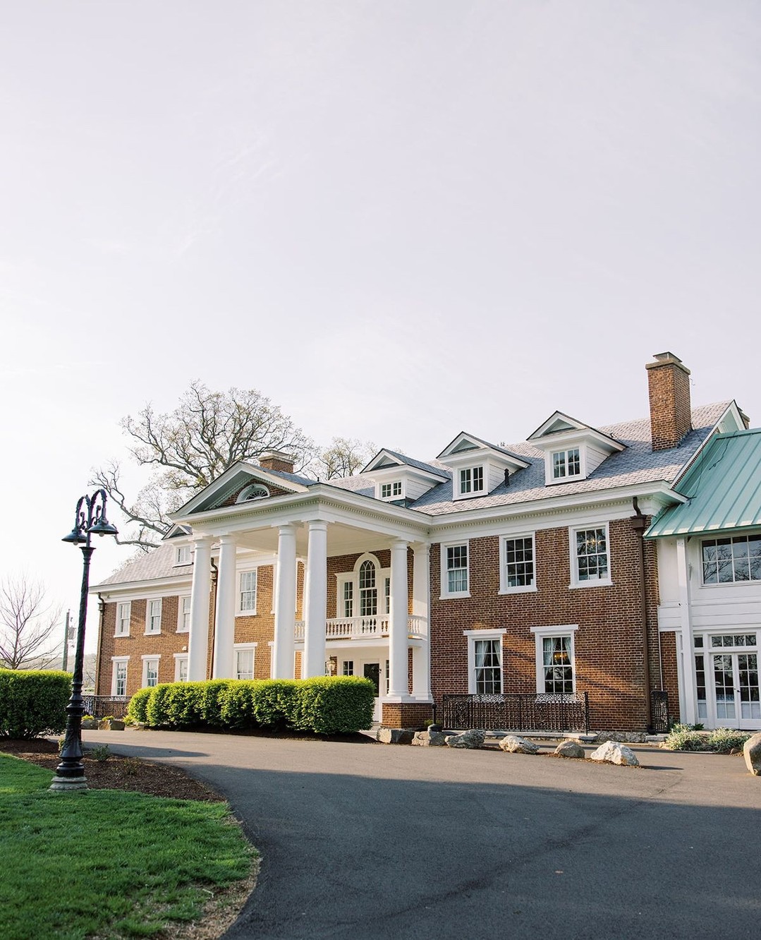 Grand brick Colonial-style mansion with white columns and green metal roof