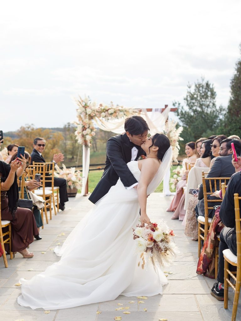 Bride and groom kissing at outdoor Virginia wedding ceremony with guests seated along stone aisle
