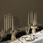 Moody tablescape with multiple lit taper candles and dark botanical centerpiece elements