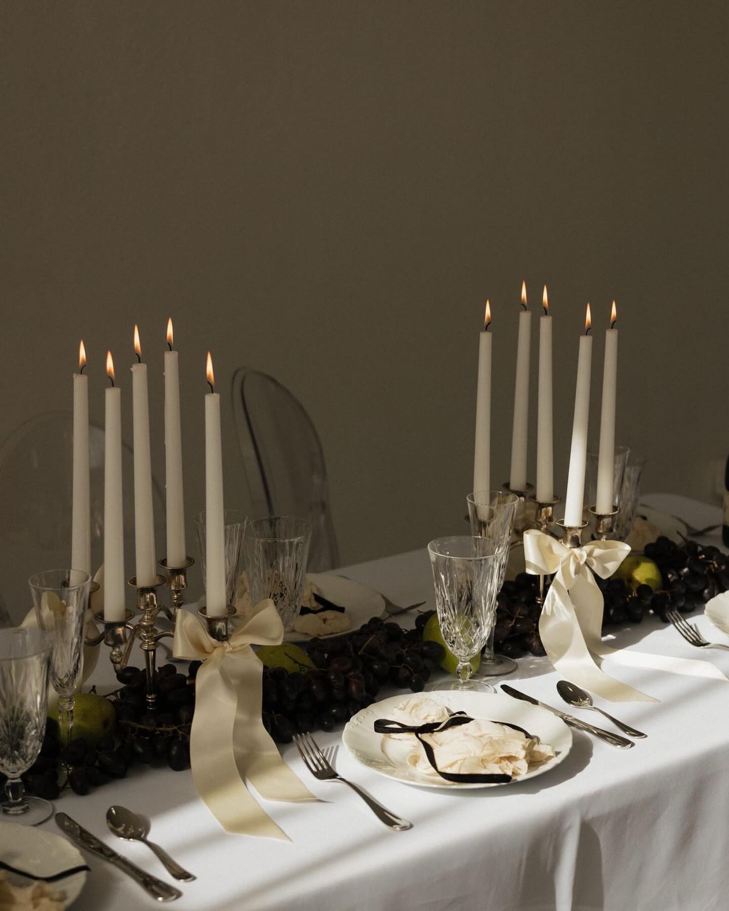 Moody tablescape with multiple lit taper candles and dark botanical centerpiece elements