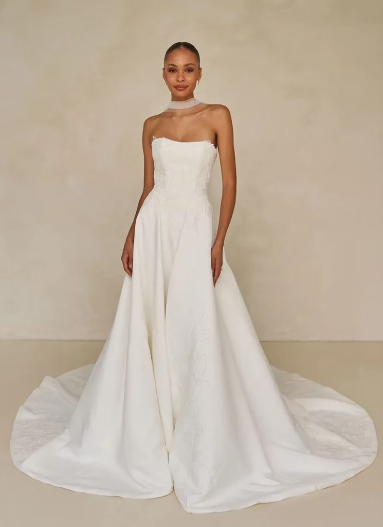 Modern bridal jumpsuit with strapless corset bodice, wide-leg pants, sheer choker detail, and dramatic cathedral train