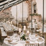 Elegant wedding reception in rustic barn with exposed brick walls, string lights, and tables decorated with tall pillar candles