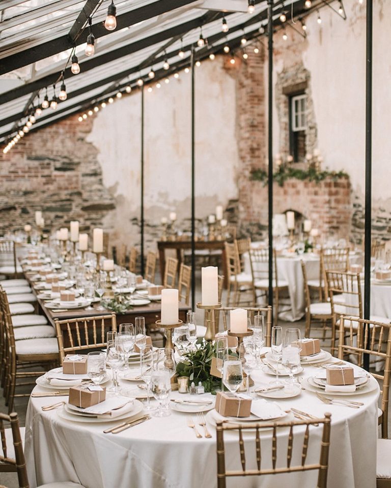 Elegant wedding reception in rustic barn with exposed brick walls, string lights, and tables decorated with tall pillar candles